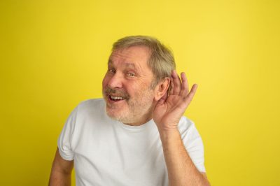 Listening to secret. Caucasian man portrait isolated on yellow studio background. Beautiful male model in white shirt posing. Concept of human emotions, facial expression, sales, ad. Copyspace.